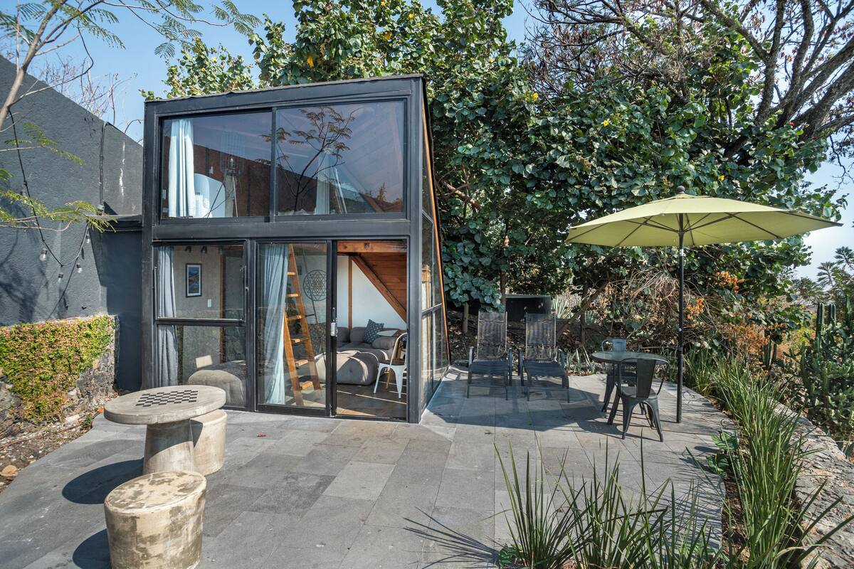 Una casa moderna con fachada de vidrio, mobiliario exterior y un gran paraguas.