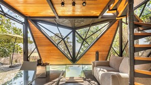 A modern interior with a glass table, a sofa, and a wooden ceiling structure. - Bosque Geométrico (Tepoztlán)