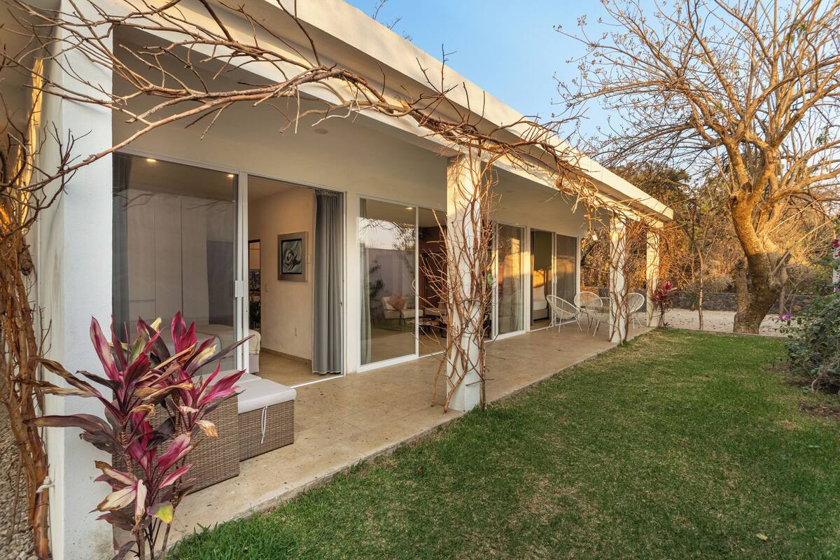 Una casa moderna con puertas de cristal amplias, un porche cubierto y un césped cuidado.