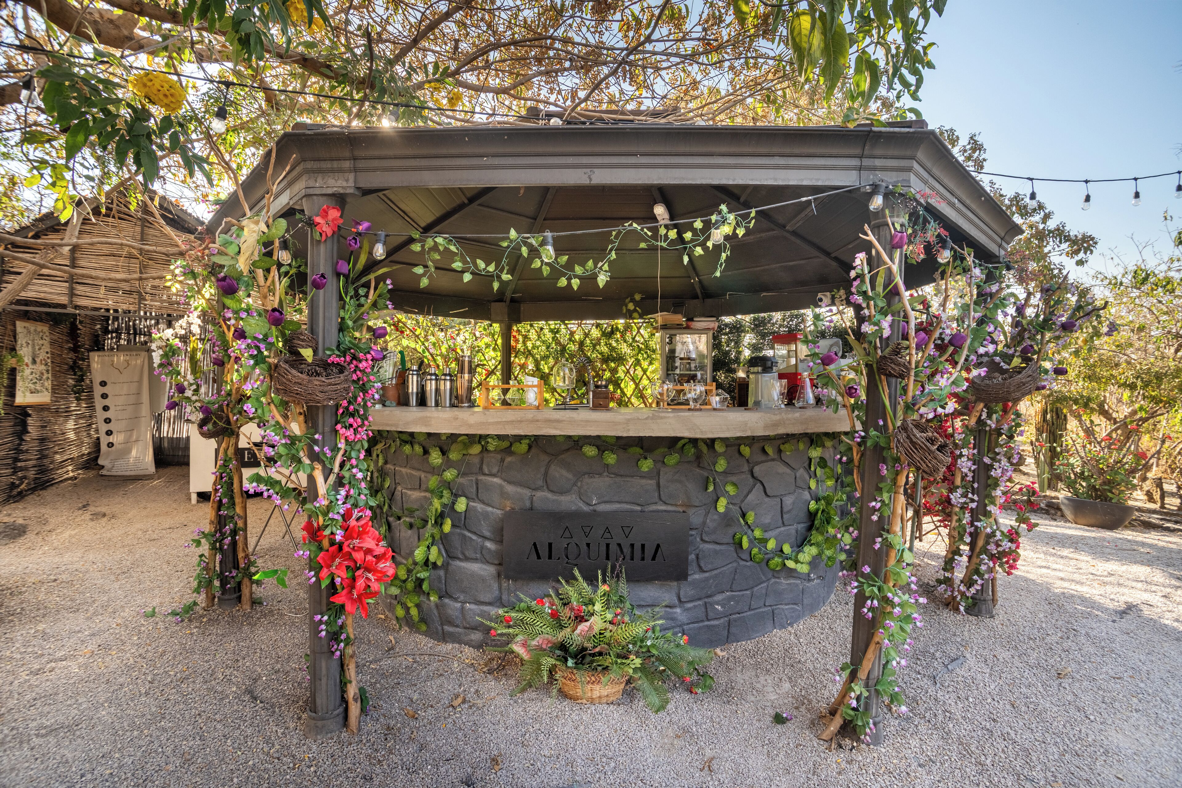 A stone structure with a sign reading 'AV AV ALOMIA,' surrounded by greenery and flowers.
