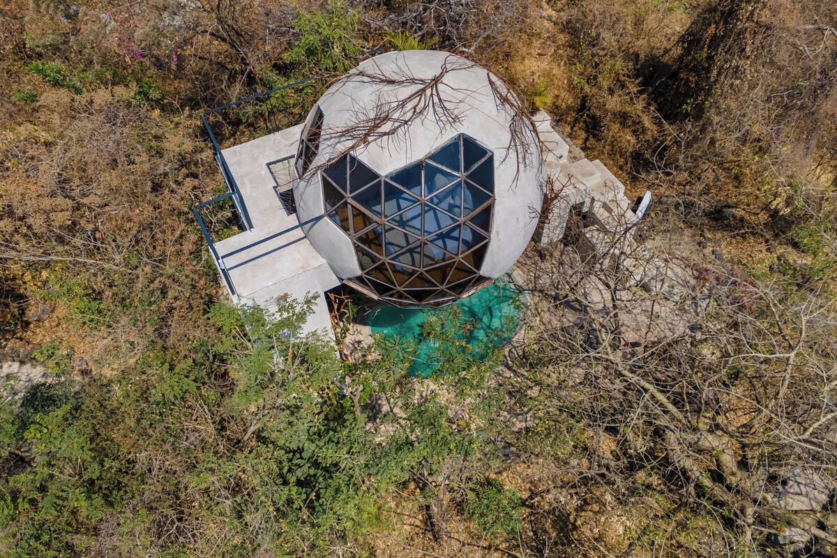 Un edificio esférico con un diseño geométrico en sus ventanas, rodeado de vegetación natural.