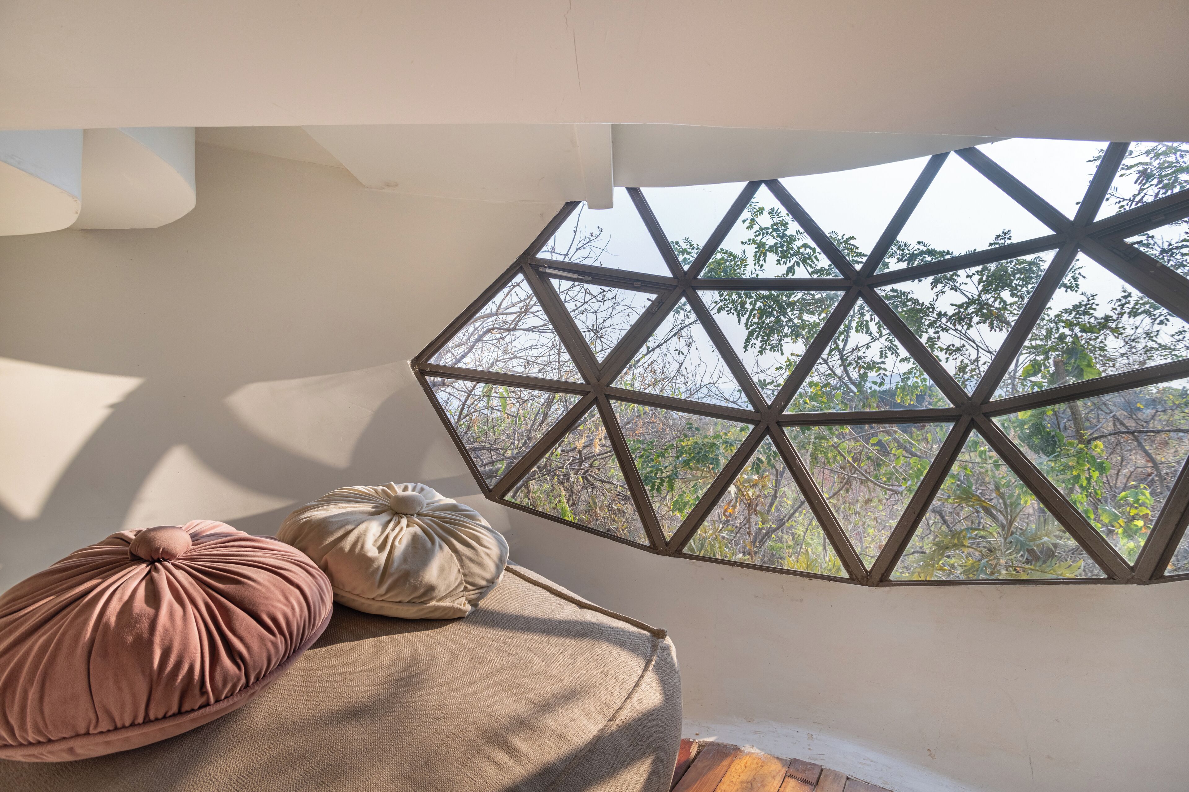 A room with a geometric window design, a bed with two pillows, and a view of trees outside.