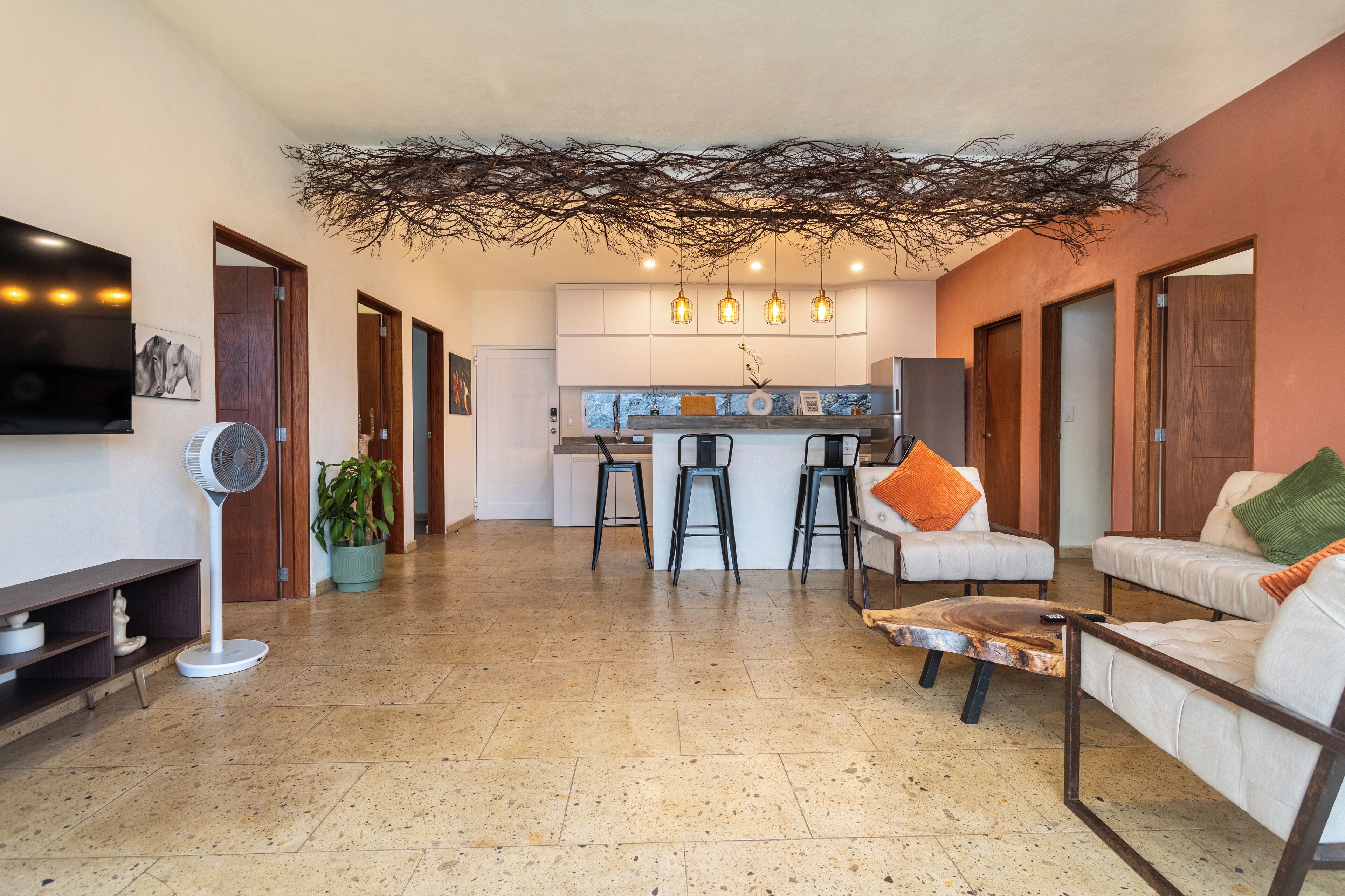 Amplia sala de estar con cocina al fondo, techo con diseño de rama natural y zona de estar con una mesa de centro.