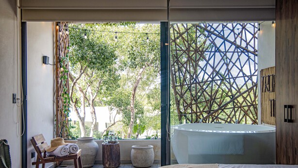 A modern bathroom with a large bathtub, a wooden chair, and a view of greenery outside. - Dk Jade 30 By Sandy Powerful (Tulum)