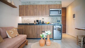 A modern kitchen with wooden cabinets, a microwave, and a coffee maker. There is a sofa with a cushion and two vases on a round table. - Dk Jade 30 By Sandy Powerful (Tulum)