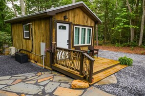 A wooden cabin with a stone-paved entrance, a small porch with a railing, and a door with a window above it.