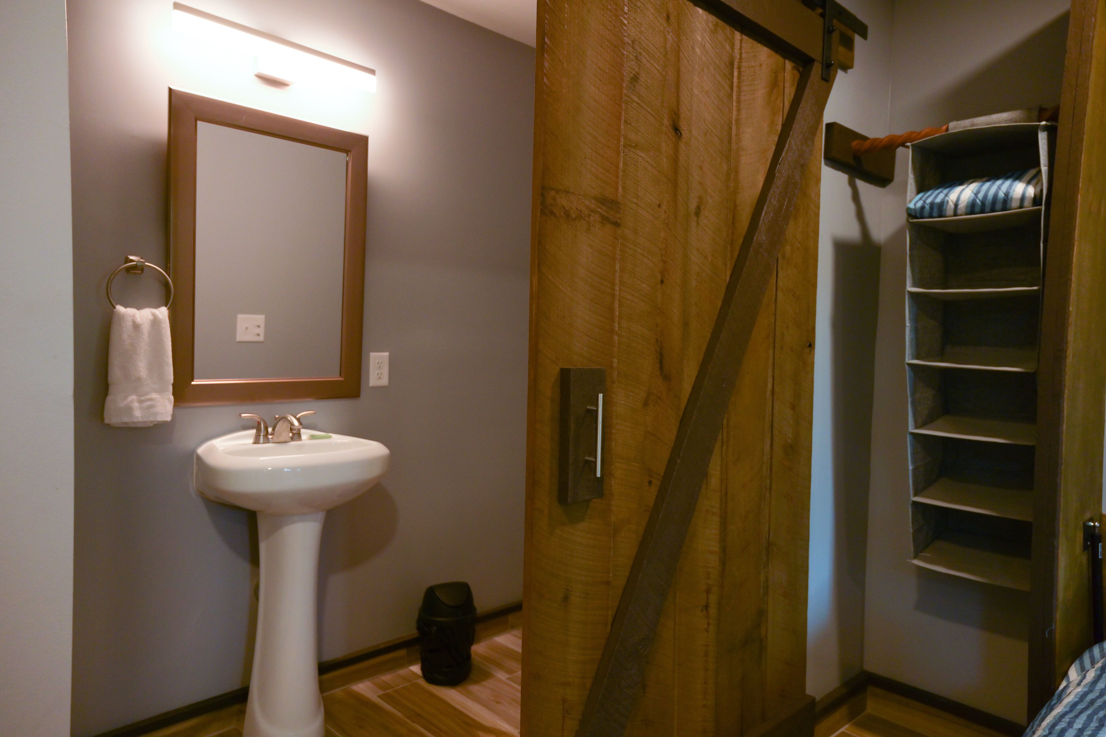 Un baño con lavamanos, espejo, toallero y puerta de madera.
