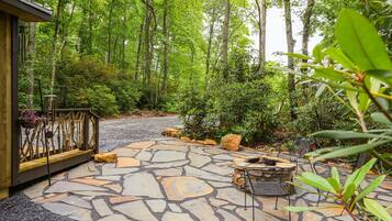 A stone patio with outdoor furniture, surrounded by lush greenery and trees.