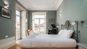 A bedroom with a large bed, a desk, a chair, and a window with a view of buildings. - T2 Flores (Porto)