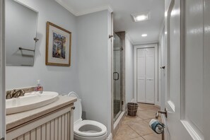 A bathroom with a white sink, toilet, and shower. There is a framed picture on the wall and a basket near the shower. - 1080 Lighthouse I at The Sea Pines Resort (Hilton Head Island)