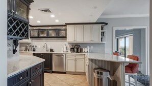 Una cocina moderna con alacenas oscuras y claras, lavavajillas de acero inoxidable y una zona de bar con un cesto de basura.