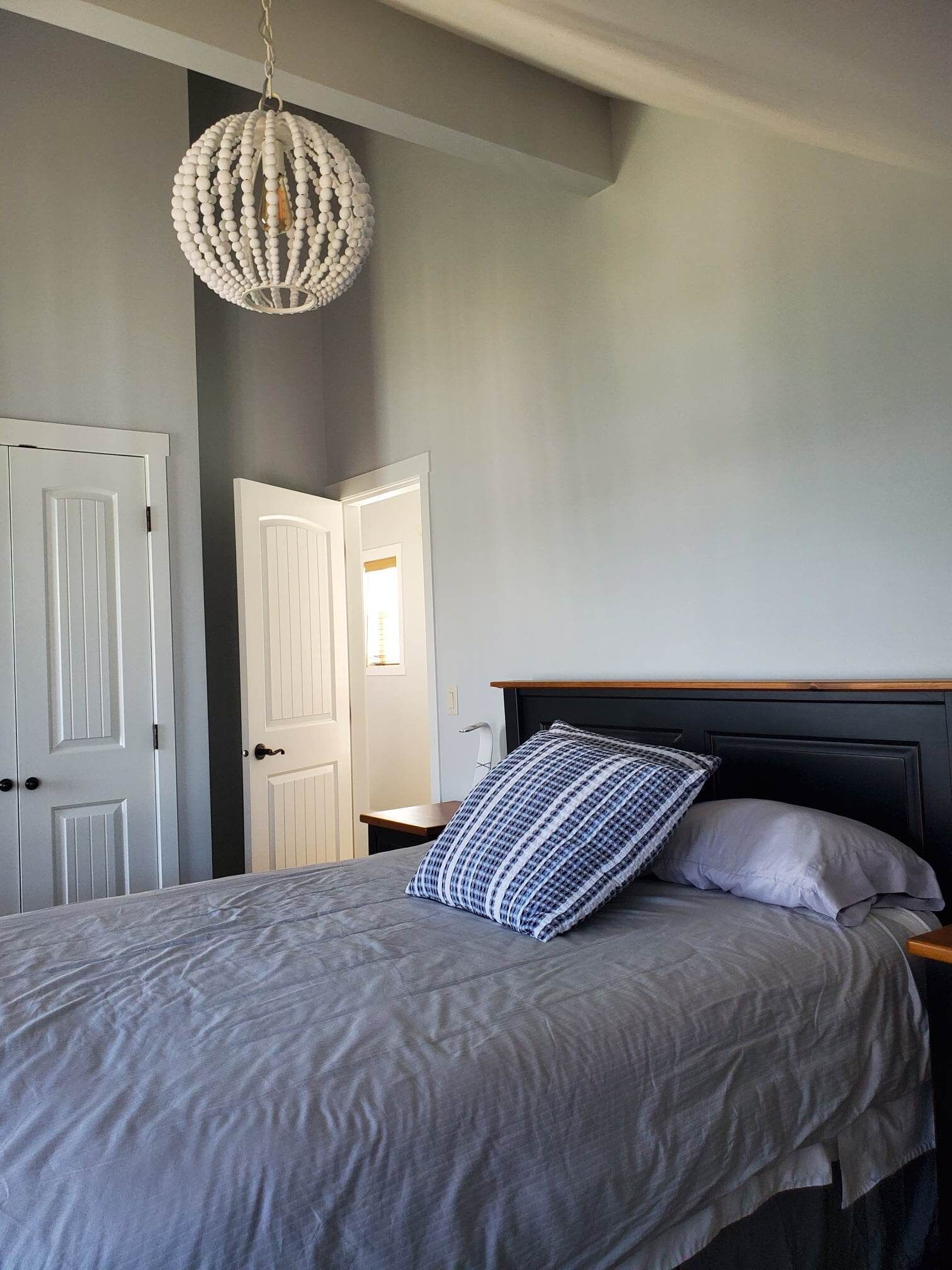 A bedroom with a bed, a bedside table, a nightstand, a hanging light fixture, and two doors.