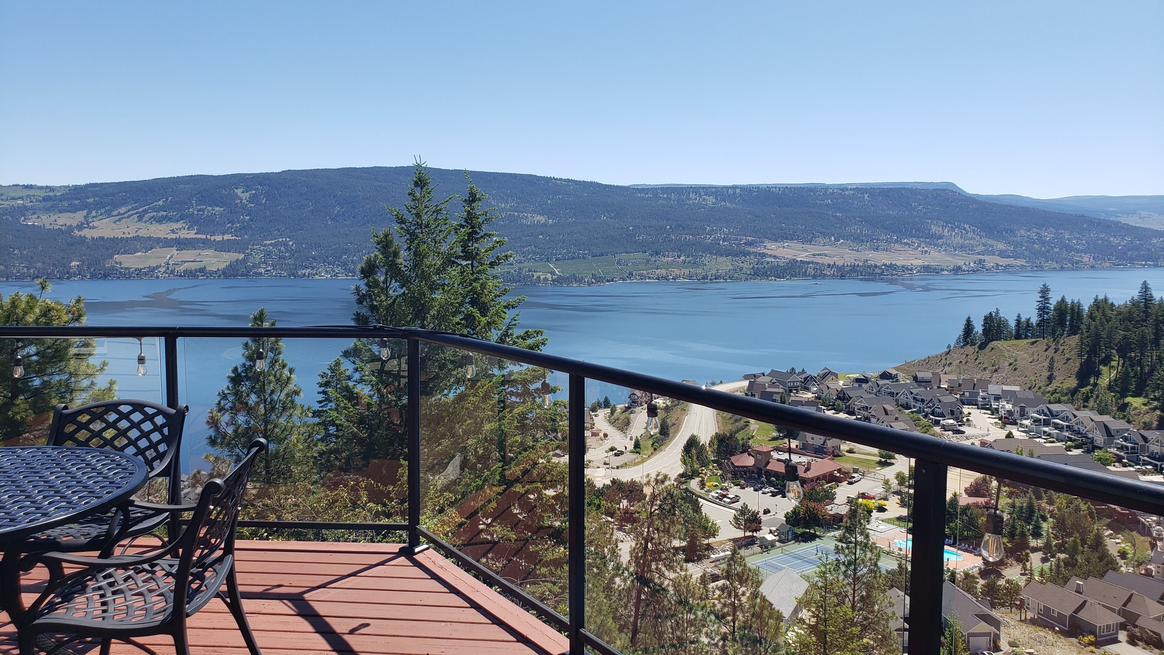 A balcony with a table and chairs overlooking a lake and residential area.