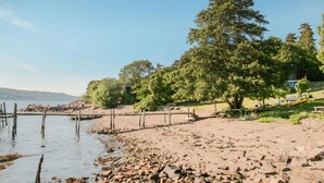 A beach with a wooden pier extending into calm waters, surrounded by trees and a grassy area with picnic tables. - Amazing home in Drøbak with kitchen (Drøbak)