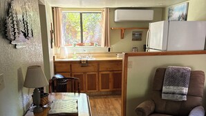 Une cuisine compacte avec des meubles en bois, une table à manger avec des chaises, un canapé et une fenêtre avec des rideaux.