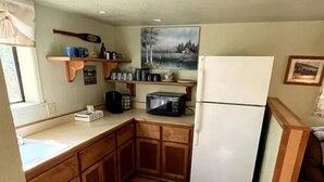 Une cuisine de taille réduite avec des meubles en bois, un réfrigérateur blanc, un four à micro-ondes et un tapis noir.