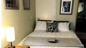 Un lit bien fait, recouvert d’une couvre-lit à motifs, avec une lampe de chevet et une petite table de nuit en bois.