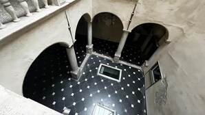 Um pátio com piso de azulejos, balaústres brancos e arcos.