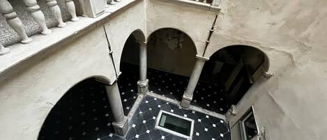 Un cortile con pavimento in piastrelle, balaustre bianche e archi.