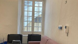 Quarto com sofá rosa, uma cadeira preta e janela com vista para um edifício.