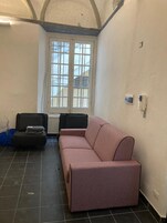 Una habitación con un sofá rosa, una silla negra y una ventana con vista a un edificio.