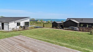 Un quartier résidentiel moderne avec une terrasse en bois, une maison blanche et une maison noire avec une voiture garée dans l’allée.