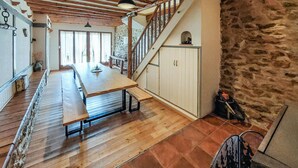 Une pièce spacieuse avec une longue table en bois, un escalier aux murs en pierre et un plafond rustique.