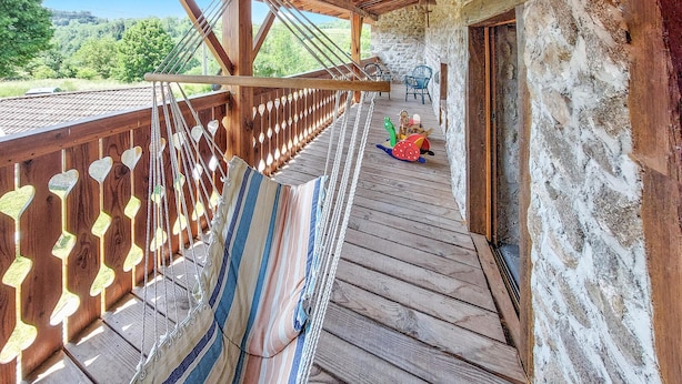Une terrasse en bois avec un hamac et des découpes en forme de cœur, un mur de pierres rustiques et une vue sur la verdure.