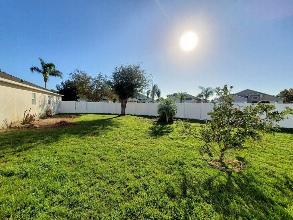 A residential backyard with a white fence, a small tree, and a well-maintained lawn.