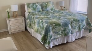 Un dormitorio con cama, mesita de noche, lámpara, un cuadro en la pared y ventana con cortinas.