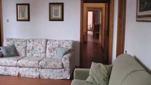 Una sala de estar con un sofá floral, un sofá verde y piso de madera. Hay dos grabados botánicos enmarcados en la pared.