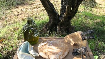Un’apparecchiatura da picnic con una pagnotta, una bottiglia d'olio d'oliva, un panno e un coltello su un tagliere di legno.