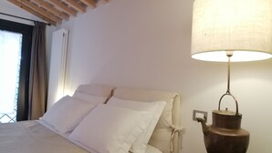 Una cama con ropa blanca, un cabecero de madera y una mesita de noche con lámpara.
