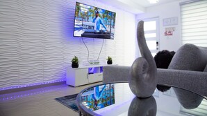 A modern living room with a flat-screen TV mounted on a textured wall, a white entertainment unit, and a glass coffee table.