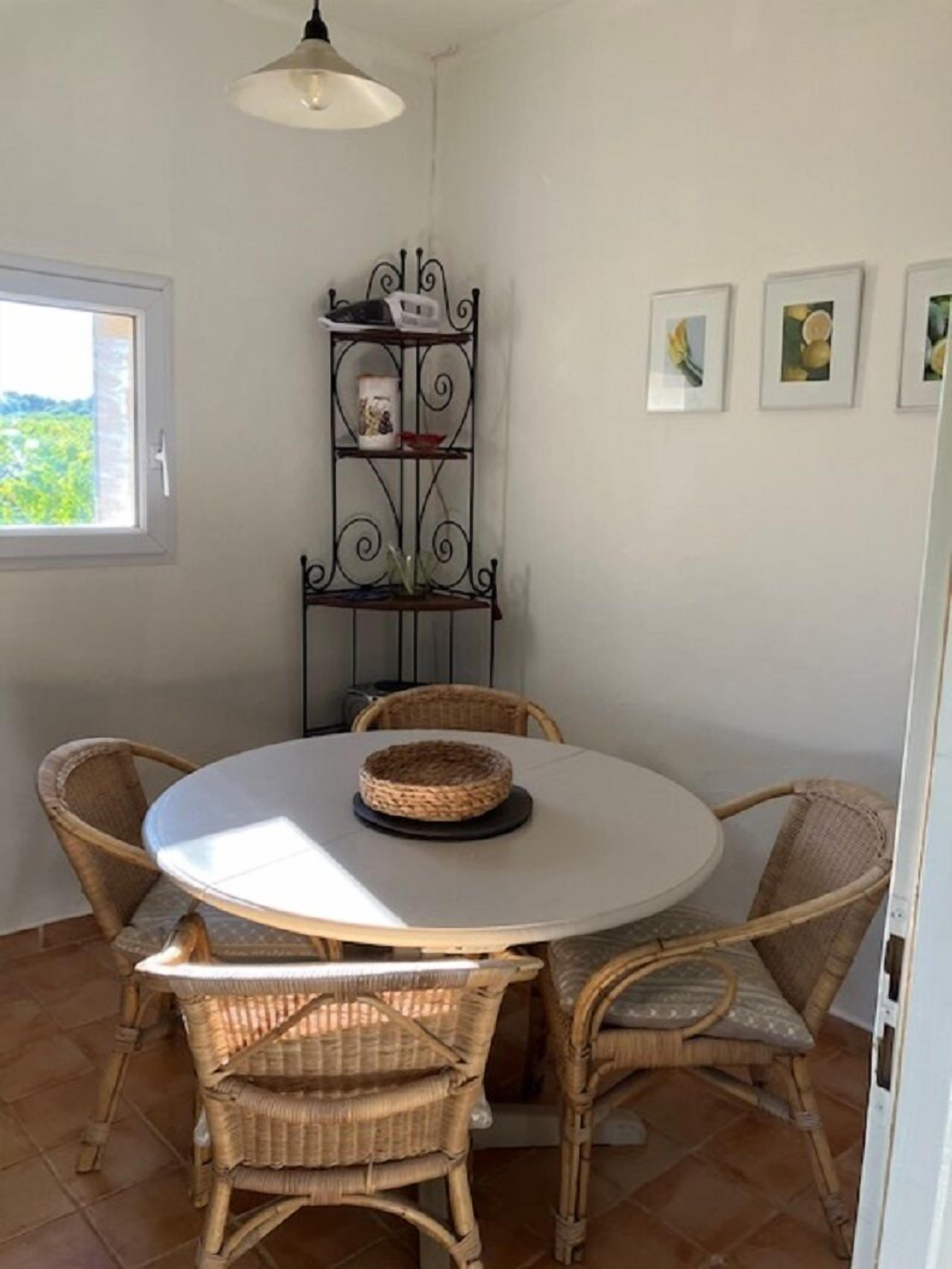 A round dining table with wicker chairs, a decorative metal shelf with items, and framed pictures on the wall.