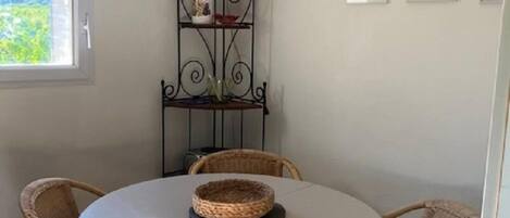 A round dining table with wicker chairs, a decorative metal shelf with items, and framed pictures on the wall.