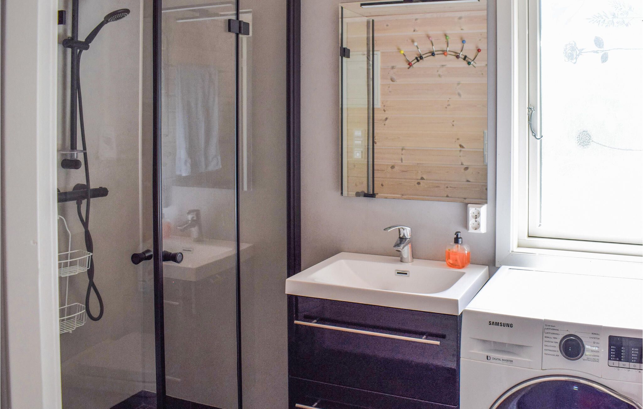 A bathroom with a glass shower enclosure, a sink with a mirror above it, and a washing machine.