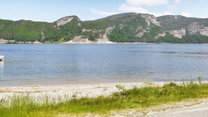 Une vue sur le lac, avec une plage de sable, des zones herbeuses et, au loin, des collines boisées.
