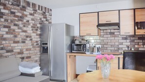Une cuisine compacte équipée d’un réfrigérateur, d’un four à micro-ondes et d’une machine à café. On y trouve une table en bois sur laquelle est posé un vase de fleurs.