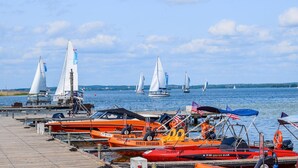 Un port de plaisance où sont amarrés différents voiliers, une jetée en bois et une étendue d’eau calme sous un ciel partiellement nuageux.