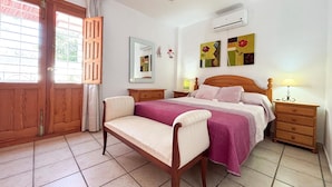 Une chambre à coucher comprenant un lit, une chaise, une table de chevet, un climatiseur et une fenêtre avec des rideaux.