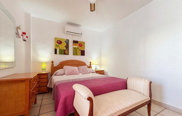 A bedroom with a wooden bed, a bedside table, a chair, an air conditioning unit, and wall art. - Stunning home in Pilar de la Horadada (Pilar de la Horadada)