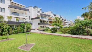 A modern residential building with multiple balconies, a well-maintained lawn, and surrounding greenery.