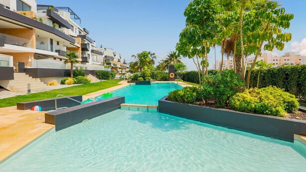 A modern residential building with a swimming pool, surrounded by lush greenery and palm trees.