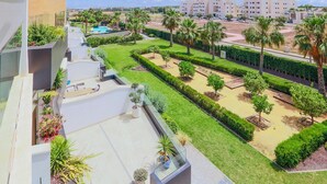 A modern residential area with a well-maintained garden, a swimming pool, and a view of the sea.