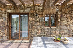Un bâtiment en pierre avec un plafond en bois, de grandes portes vitrées et des plantes en pot disposées sur un sol carrelé.