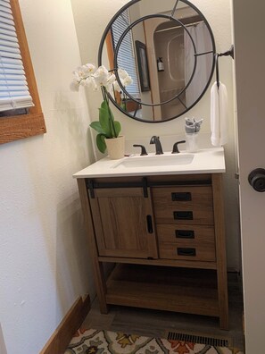A bathroom with a wooden vanity, a round mirror, a white sink, and a potted orchid.