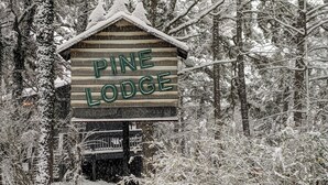 Lumisen metsän keskellä oleva opaste, jossa lukee Pine Lodge.