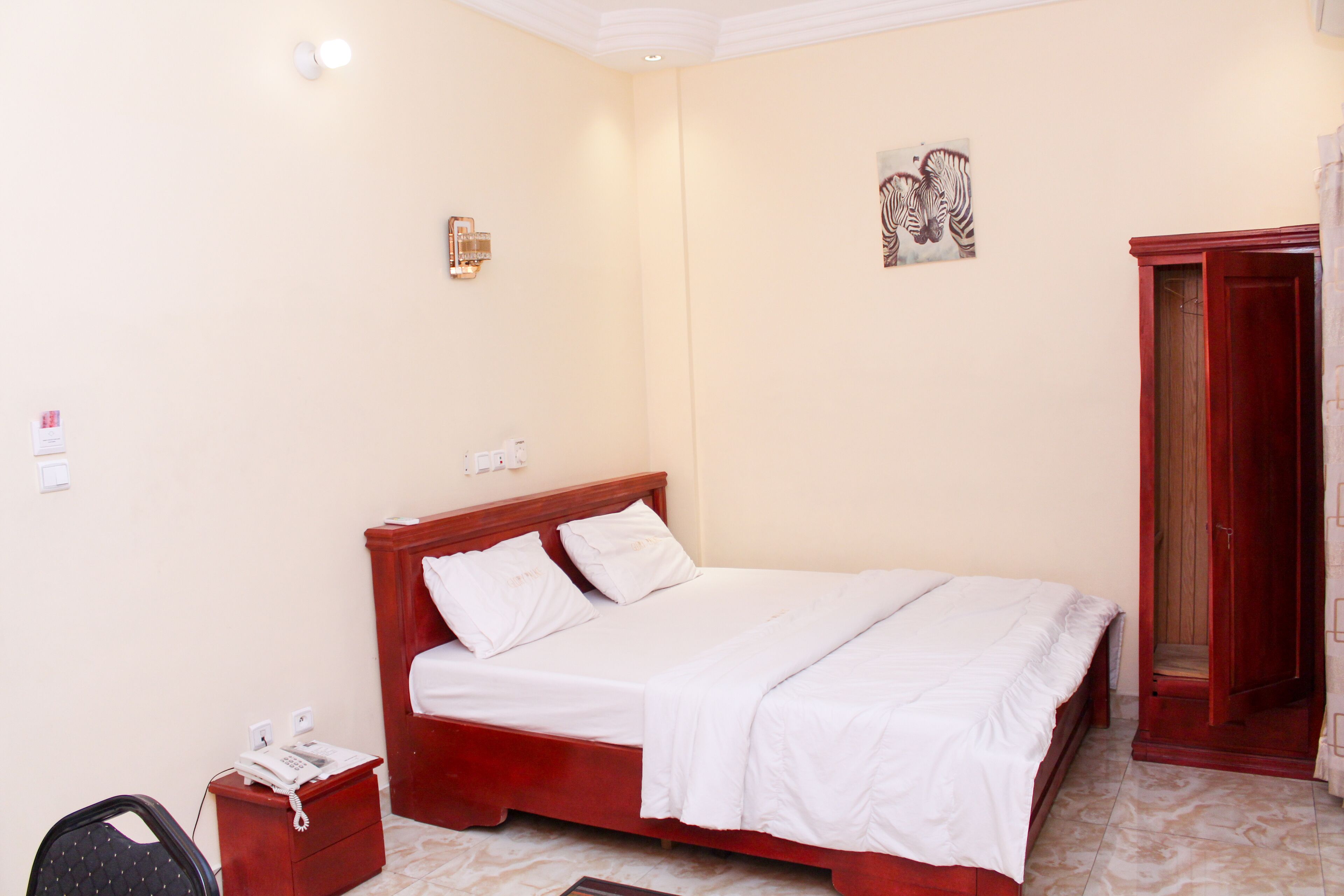 Cama bem arrumada em quarto com cabeceira de madeira, mesa de cabeceira pequena com telefone e guarda-roupa vermelho.