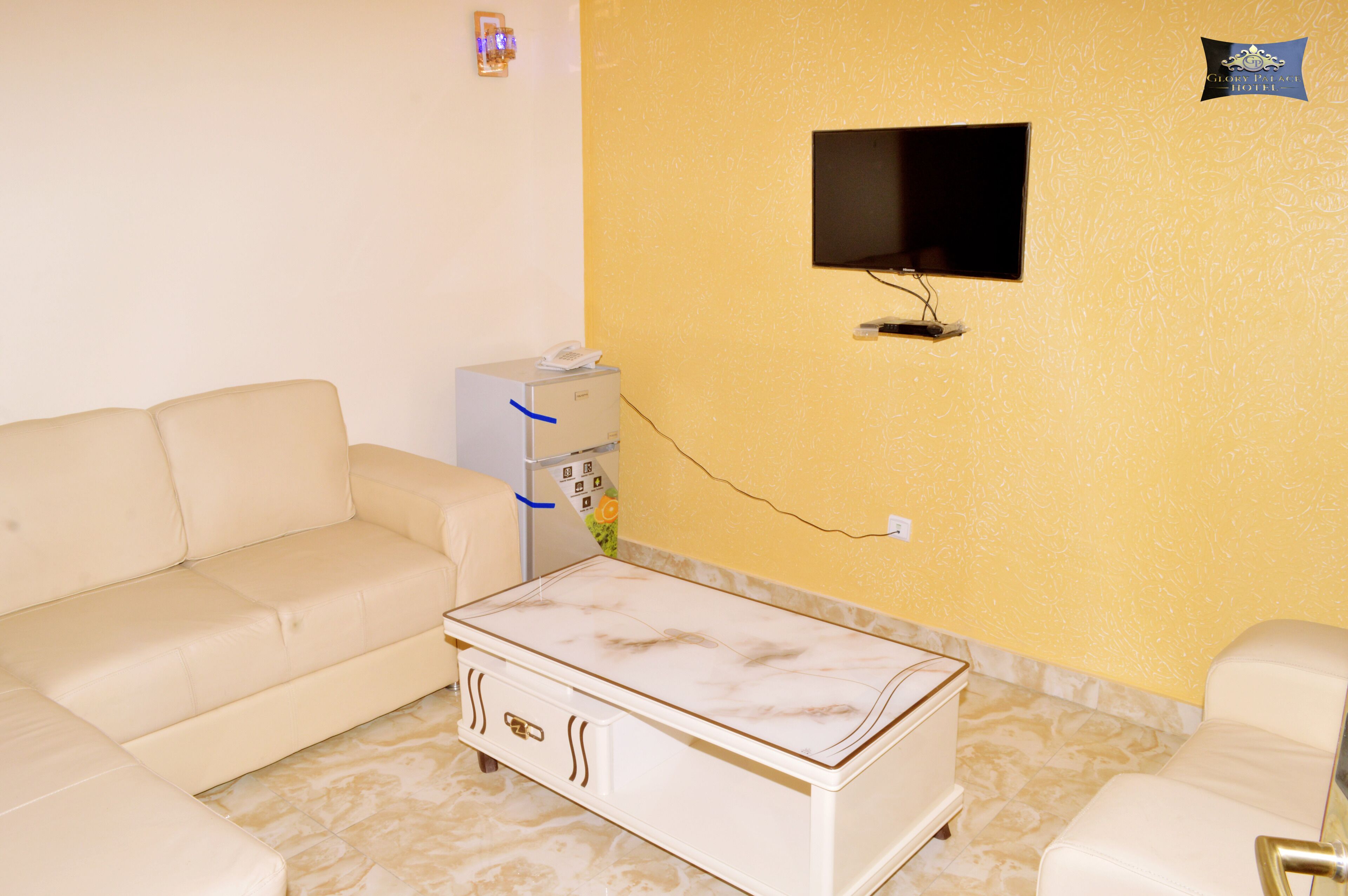 A room with a white sofa, a white coffee table, a flat-screen TV mounted on the wall, and a small desk with a telephone.